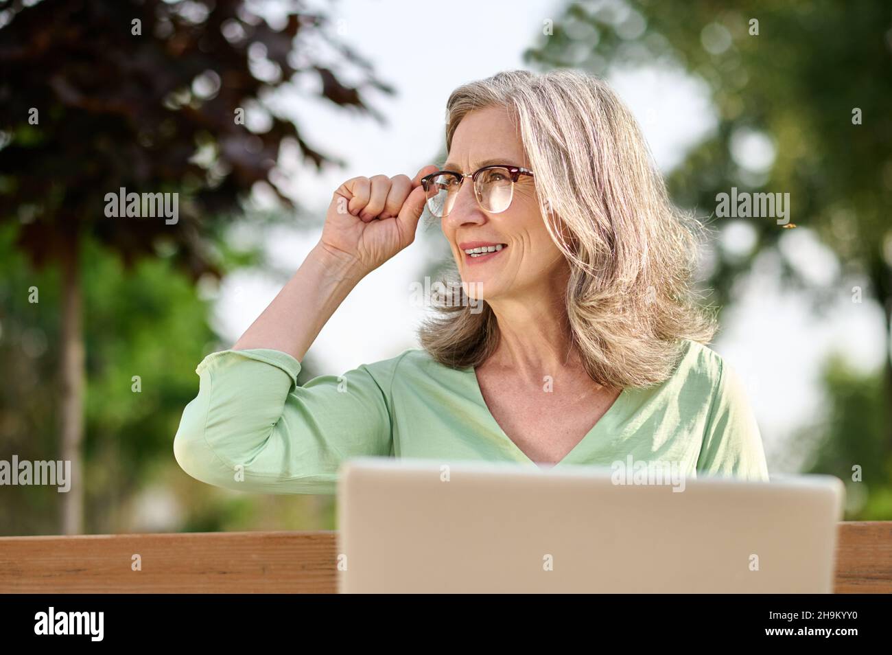 Frau mit Laptop, die auf der Bank zur Seite schaut Stockfoto