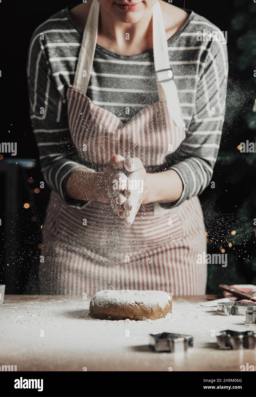 Frohe Weihnachten, Frohes neues Jahr. Lebkuchenkochen, Kuchen, Strudelbacken. Die Frau im Vorfeld bereitet Kekse vor. Handflächen schlagen, Mehl über den kneteten Teig spritzen. Junges Mädchen vorbereiten, backen, kochen Stockfoto