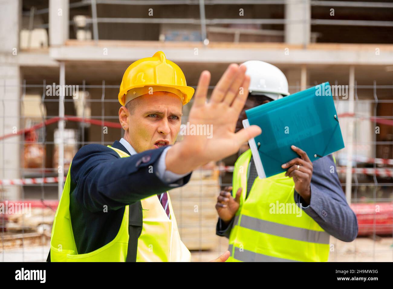 Der Vorarbeiter verbietet das Fotografieren auf der Baustelle, indem er das Kameraobjektiv schließt Stockfoto