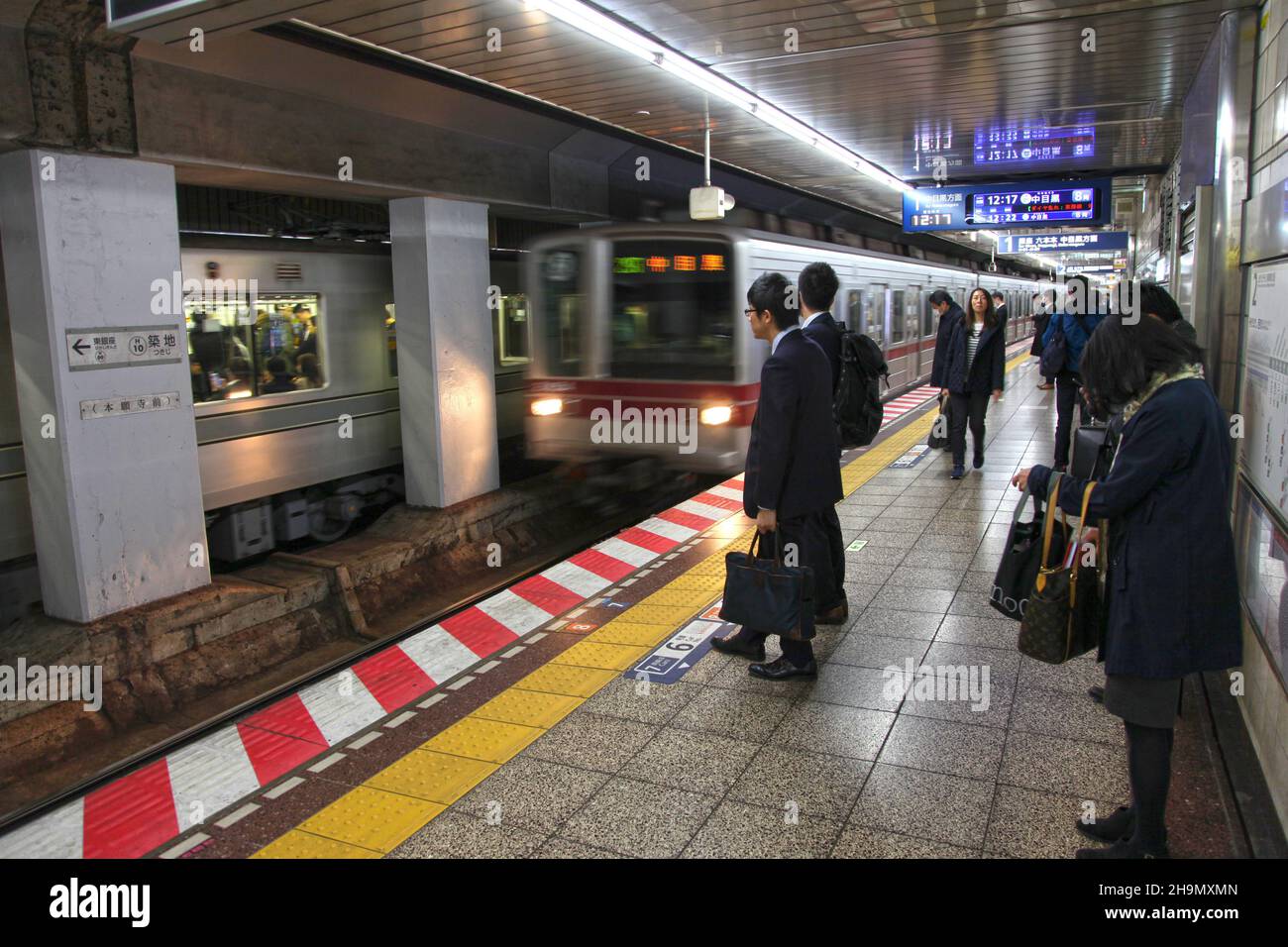 Ein Zug, der am Bahnhof Tsukiji anfährt, mit vielen Pendlern auf dem U-Bahnsteig in Tokio, Japan. Stockfoto