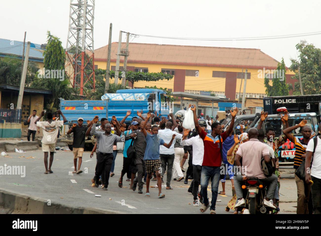 Lagos, Nigeria, 7th. Dezember 2021. Passanten heben ihre Hände, während sie an Polizeifahrzeugen am Gymnasium in Ojodu, Lagos, Nigeria, vorbeigehen, wo ein Lieferwagen, der angeblich von Verkehrsbeamten gejagt wurde, einige Schüler tötete, die von der Schule zurückkehrten. Während der Augenzeuge sagte, dass mindestens 17 Schüler starben, bestätigte die Polizei am Dienstag, dass drei Tote, 12 Verletzte, bei dem Unfall starben. Foto von Adekunle Ajayi Stockfoto