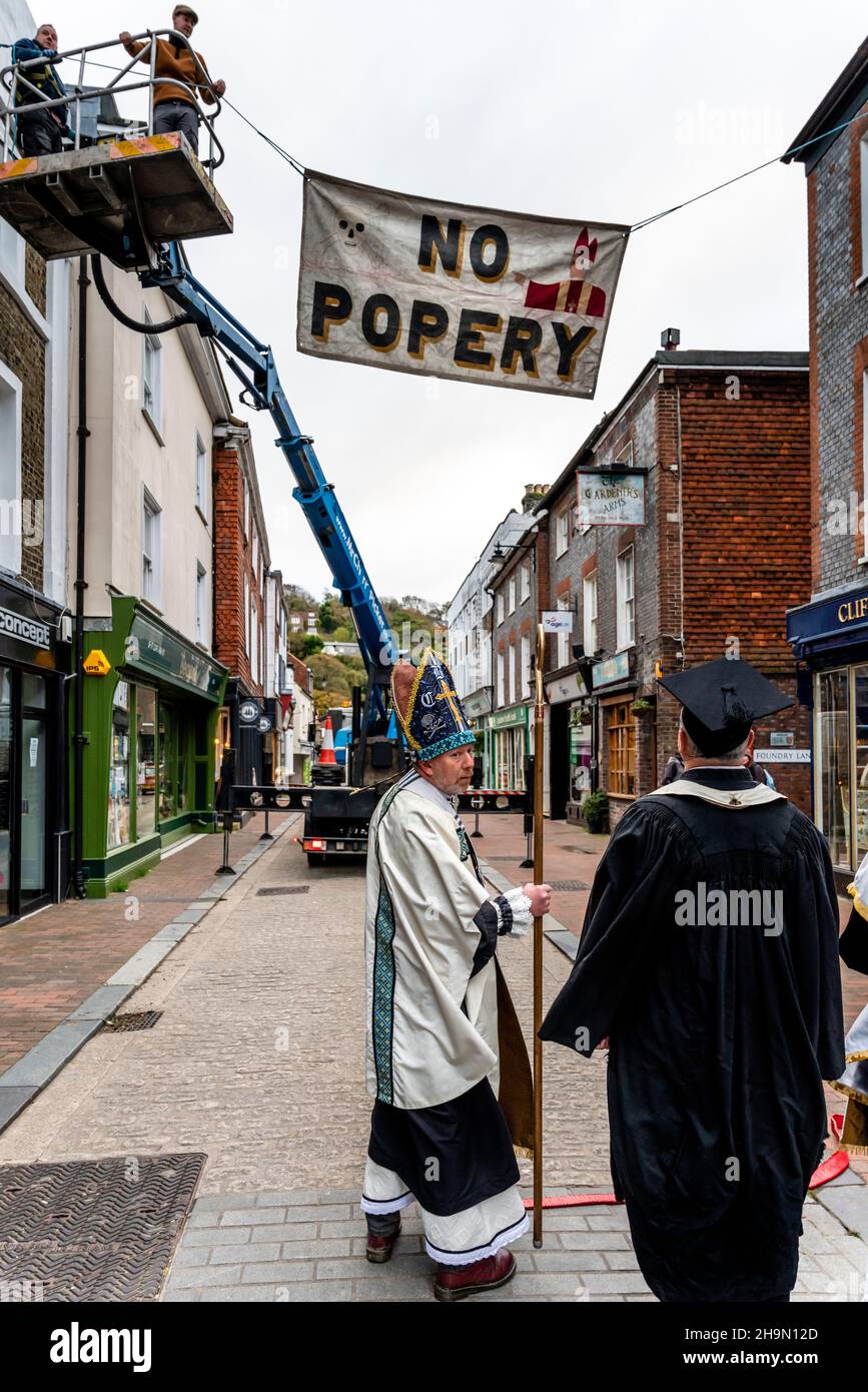 Mitglieder der Cliffe Bonfire Society in religiösem Kostüm Uhr als traditionelle Zeichen und Banner werden in den Straßen, Lewe, Sussex, Großbritannien, aufgesetzt. Stockfoto