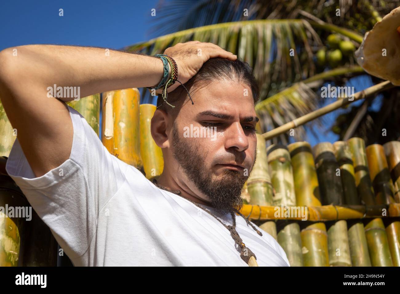 Junger Mann mit der Hand auf dem Kopf und ernstem Ausdruck, der nach unten blickt. Stockfoto