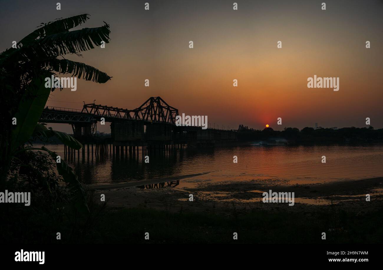 Sonnenuntergang über der Long Bien Brücke die Long Bien Brücke wurde 1902 von den Franzosen über den Roten Fluss in Hanoi, Vietnam, gebaut. Dies ist eine der ältesten Brücken Stockfoto