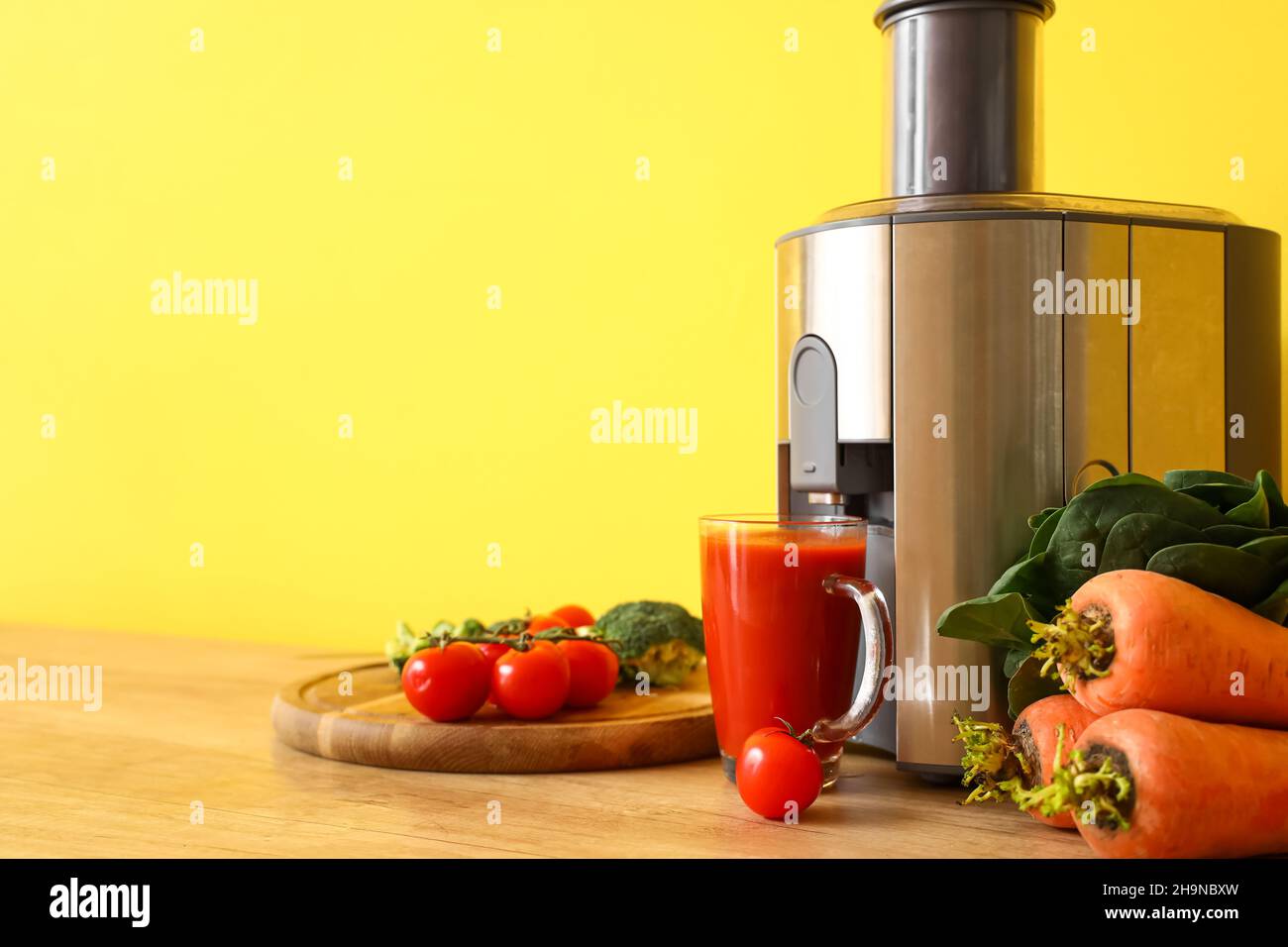 Moderner Entsafter mit frischem Gemüse und einer Tasse Saft auf dem Tisch in der Küche Stockfoto