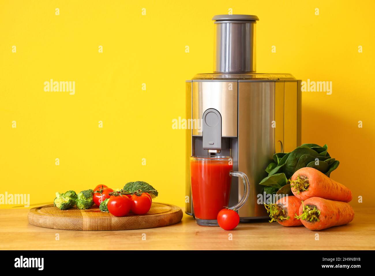 Moderner Entsafter mit frischem Gemüse und einer Tasse Saft auf dem Tisch in der Küche Stockfoto