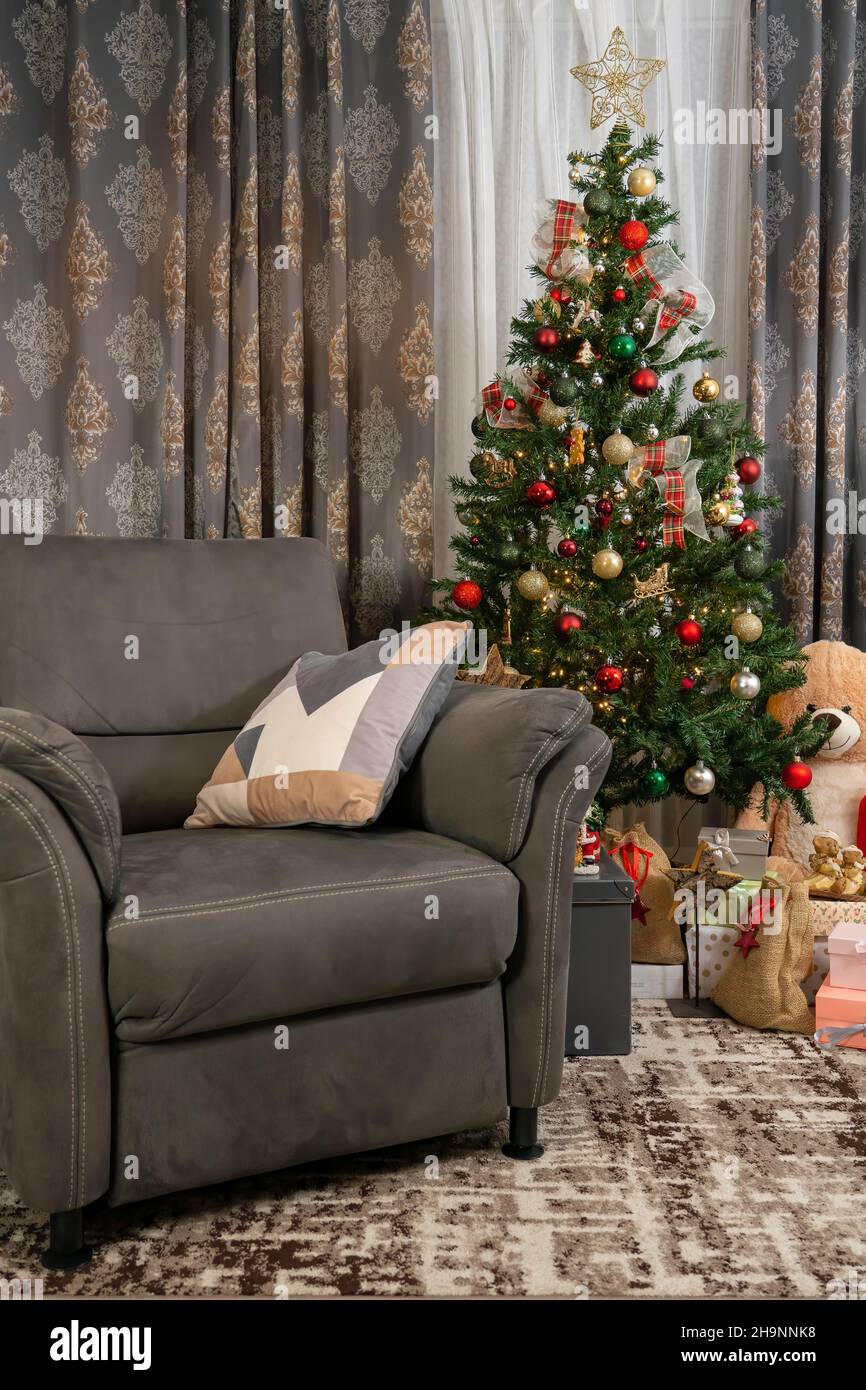 Wohnzimmer mit einem Sofa für eine Person und Weihnachtsbaum und Geschenkboxen und Spielzeug eingerichtet. Stockfoto