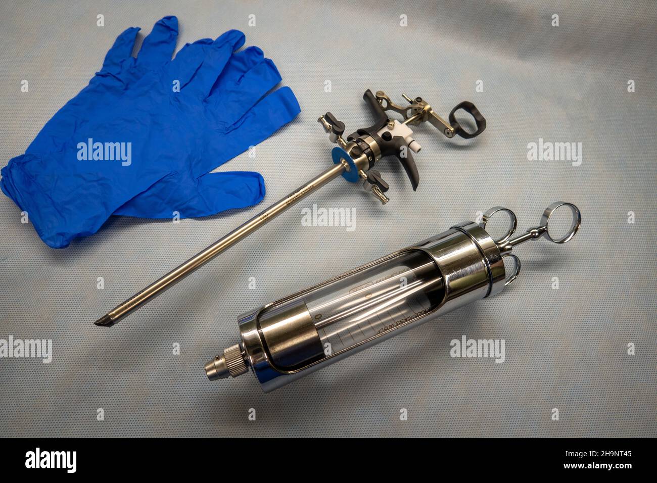 Ein Instrument zur Durchführung einer Prostataresektion liegt neben blauen medizinischen Handschuhen und einer Glasspritze Stockfoto