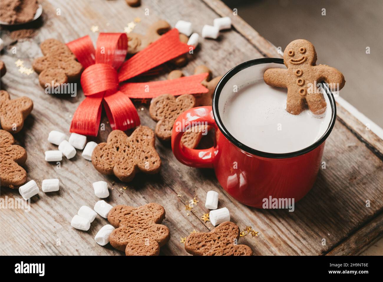 Ingwer in einer Tasse Kakao mit einer großen roten Schleife auf einem Holzhintergrund, Draufsicht. Verschiedene Weihnachtsbonbons mit einer Tasse Kakao auf dem Tisch. Weihnachten Stockfoto