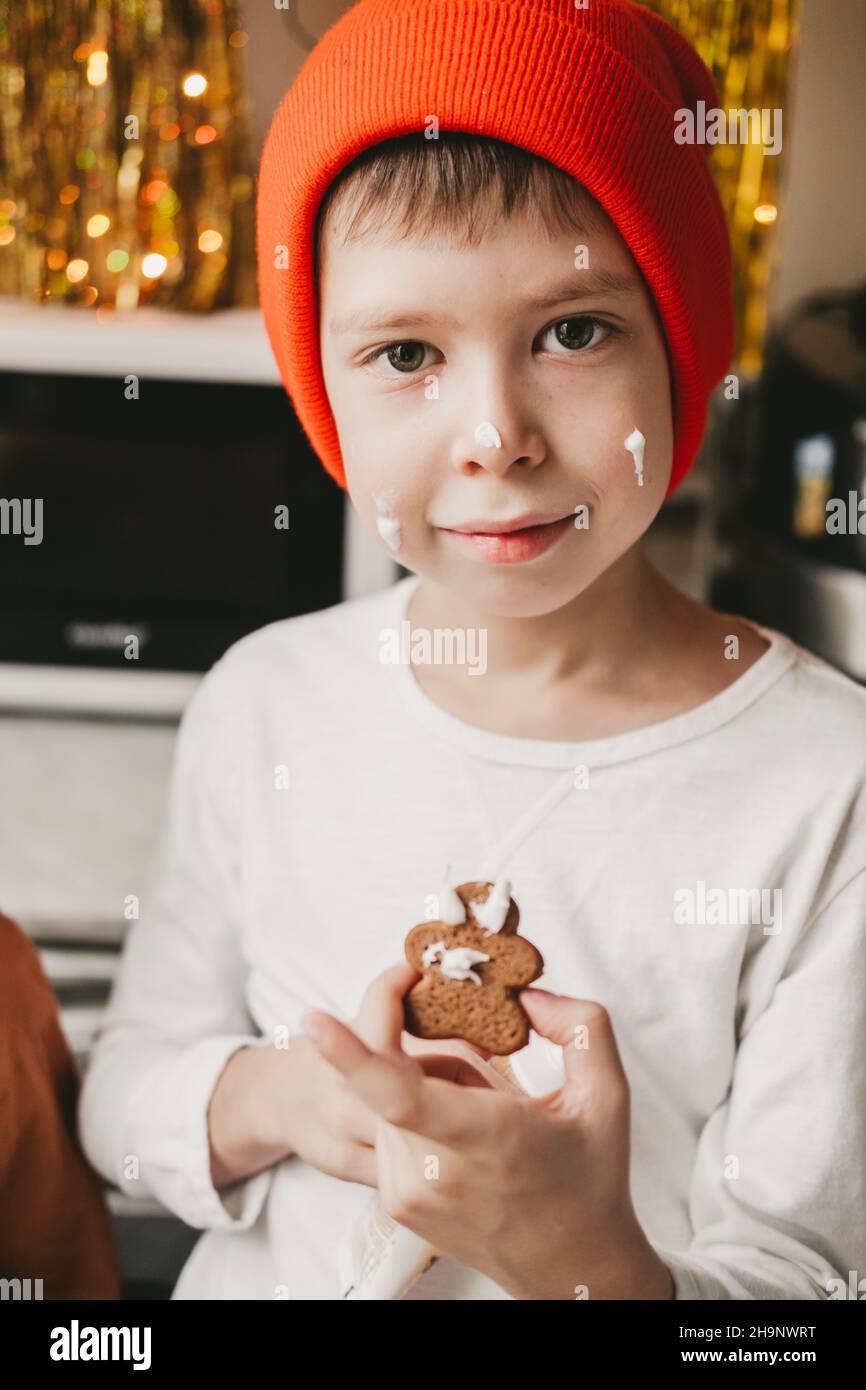 Junge dekorieren Weihnachtskekse mit weißer Glasur. Kinder schmücken einen Lebkuchenmann auf einem hölzernen Hintergrund. Weihnachtsbonbons mit Kakao und Marschmall Stockfoto