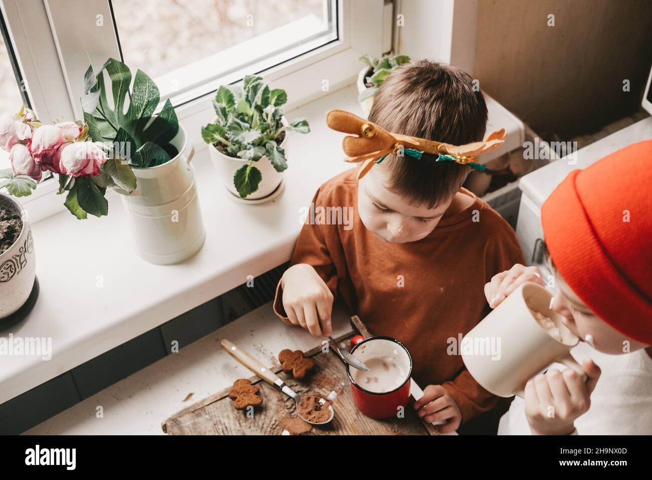 Kinder trinken Kakao mit Salmler und weihnachtslebkuchenmann auf einem hölzernen Hintergrund. Winterurlaub zu Hause. Lustige Zeit in der Küche. 2 Jungen Stockfoto