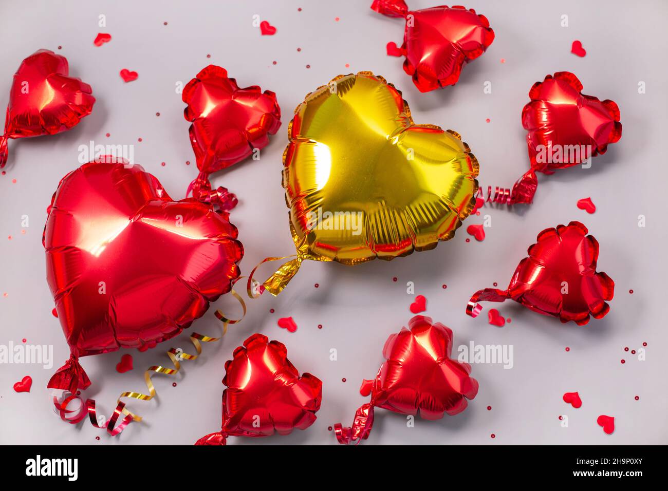 Rote und goldene Luftballons aus herzförmiger Folie auf grauem Hintergrund. Metallballon. Liebeskonzept. Feiertagsfeier. Dekoration zum Valentinstag oder zur Party. Stockfoto