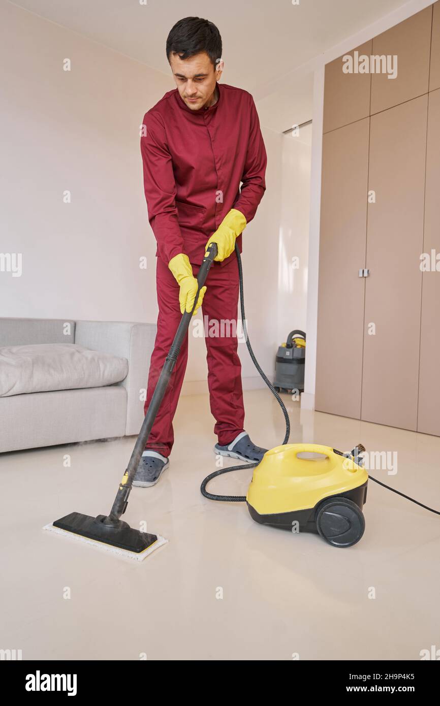 Konzentrierter Hausierer in Gummihandschuhen mit Dampfreinigungsgerät Stockfoto