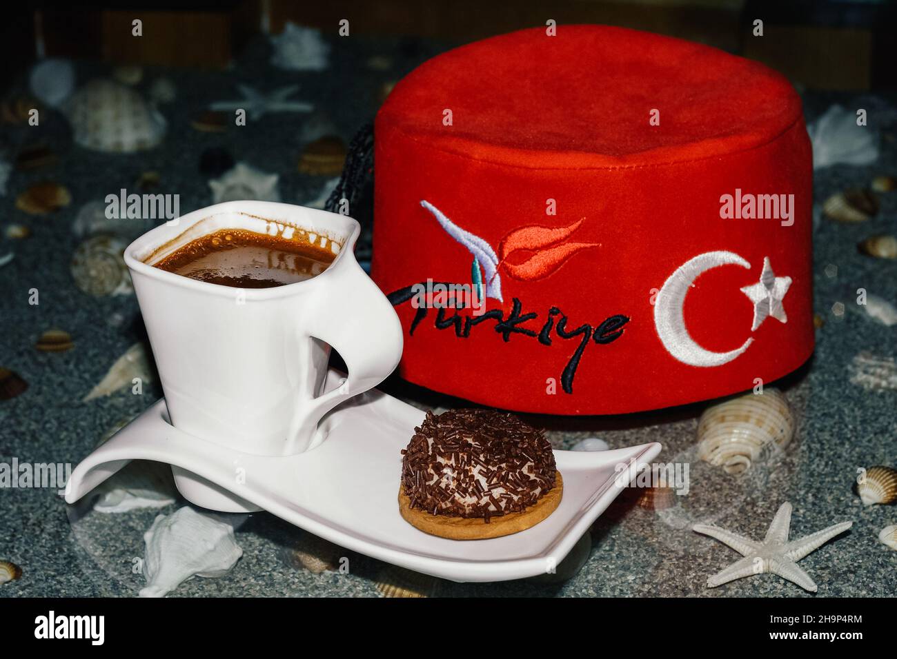 Türkischer Kaffee und Keks mit fez auf dem Tisch mit Meersand. Weiße Kaffeetasse mit rotem türkischen Hut Stockfoto