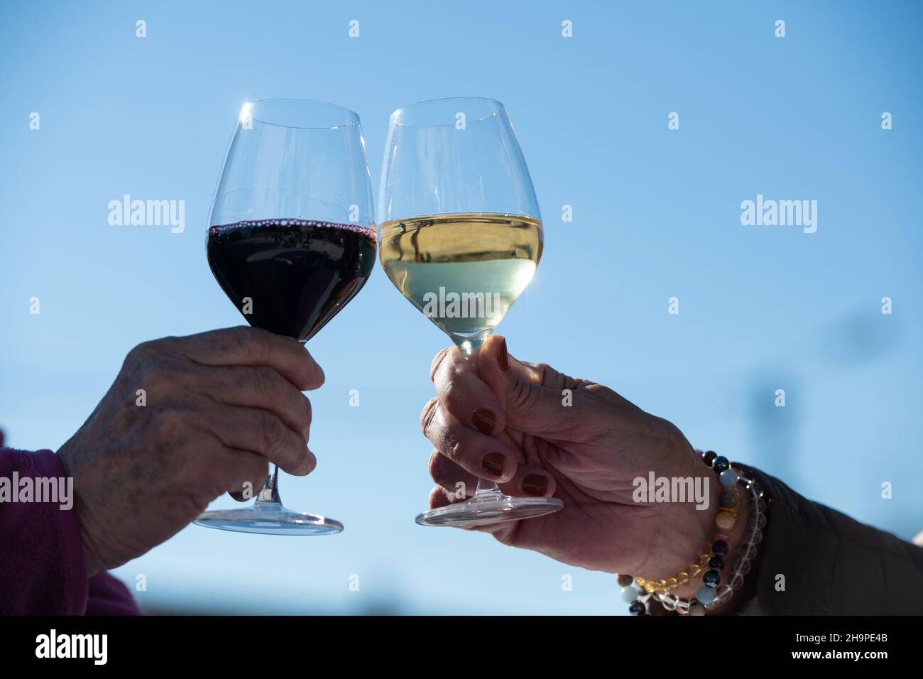 Zwei Personen klirren Gläser mit Rot- und Weißwein. Hand eines Mannes und einer Frau, die ein Glas Wein in der Hand halten Stockfoto