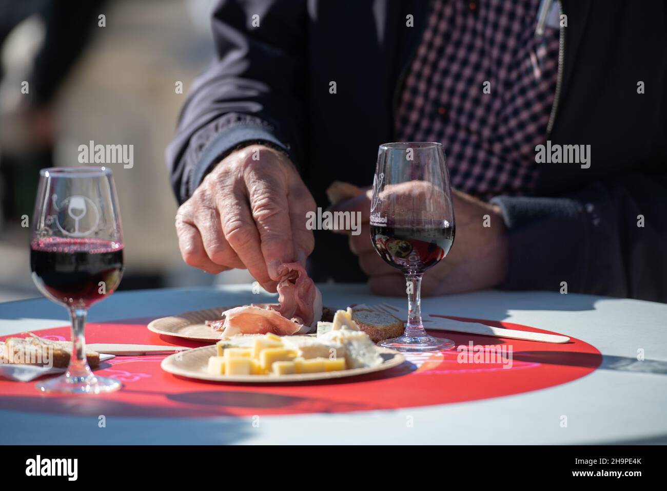 Mann beim Essen von gekochtem Schweinefleisch und Gläsern Rotwein auf einem Tisch während eines Workshops „Apero sur un Plateaus, Vins & Fromages“ (Wein- und Käseverkostung) in Stockfoto