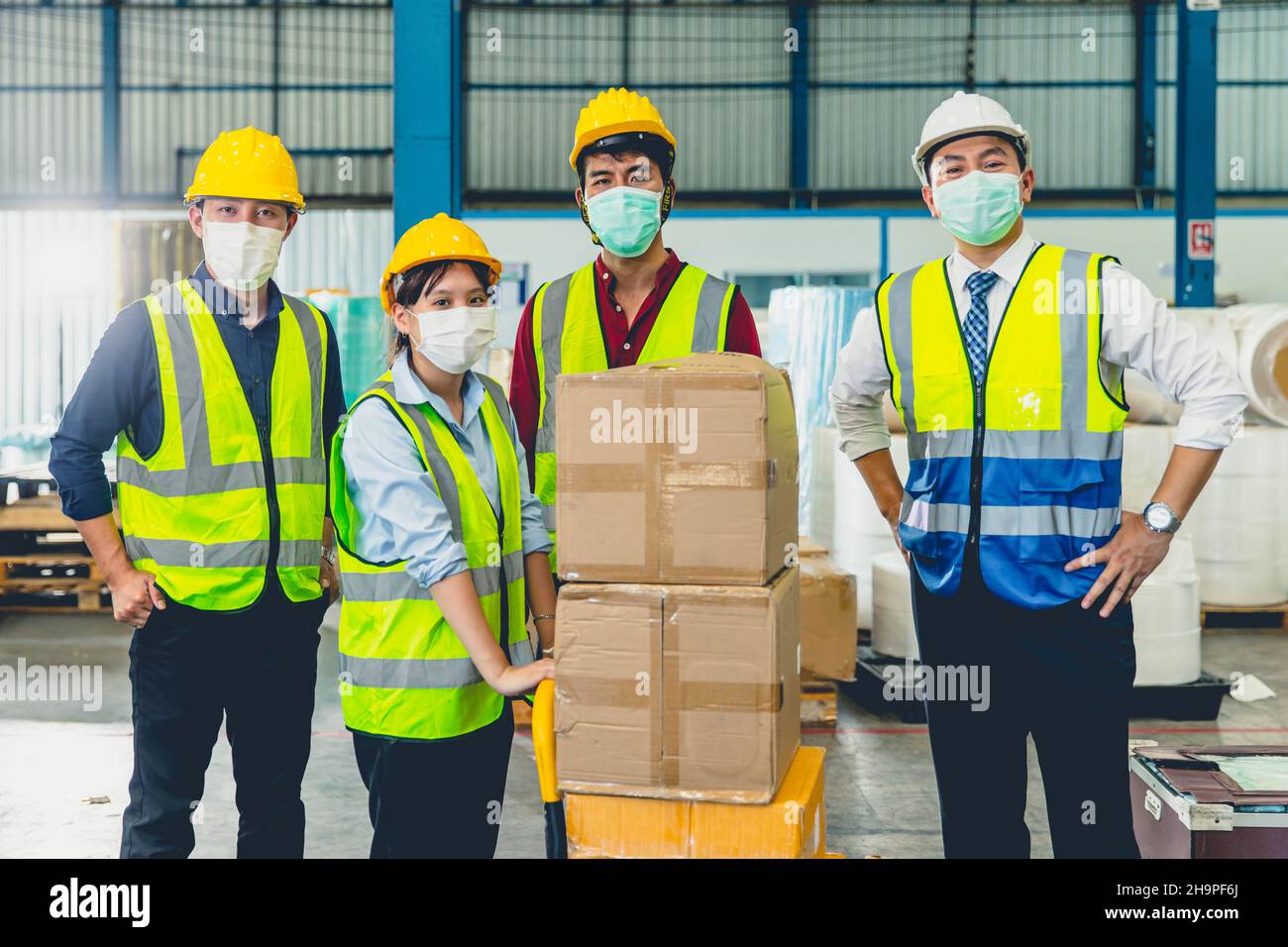 Eine Gruppe asiatischer Teamarbeiter trägt eine Gesichtsmaske, die im Lagerhaus zusammensteht Stockfoto