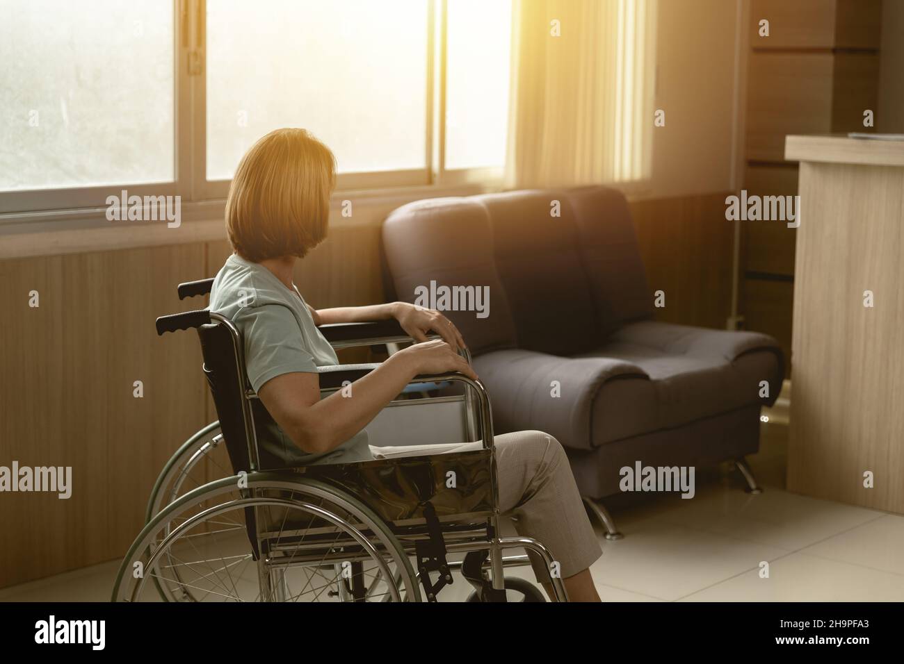 Patient, der allein auf dem Rollstuhl sitzt und mit Hoffnung auf das Krankenhaus oder das Pflegefenster schaut. Stockfoto