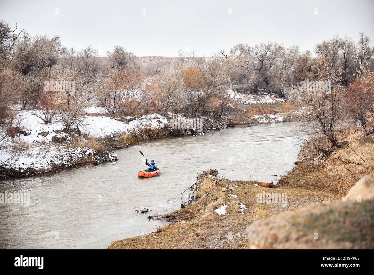 Im Winter paddelt der Mensch auf einem orangefarbenen Floßboot im Fluss. Stockfoto