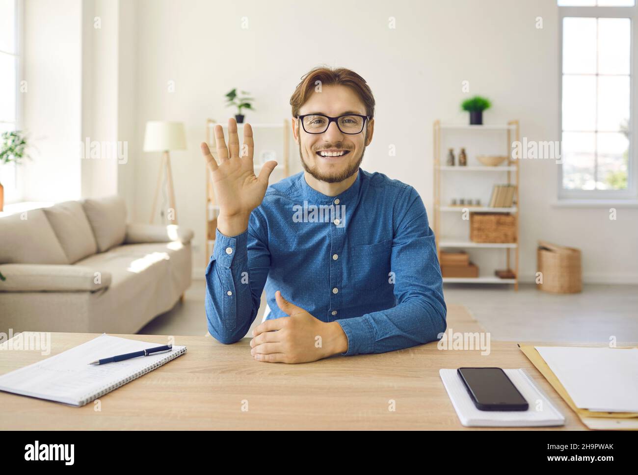 Freundlicher junger Mann, der seine Hand vor der Webcam schwenkt und die Teilnehmer zu einem Online-Meeting begrüßt. Stockfoto