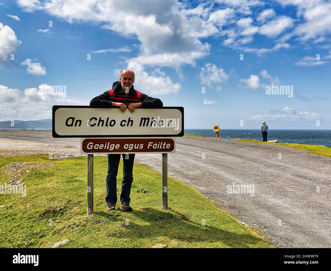 Tourist lehnt sich gegen Willkommensschild in irischer Sprache, Inschrift Gaeilge Agus Failte, Panorama Atlantic Drive, südliche Achill Island, Mayo, Wild Atlantic Stockfoto