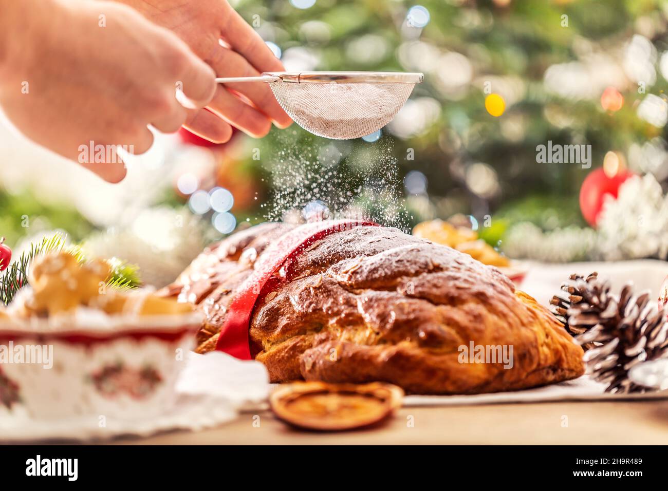 Detail der Hände, die das Sieb halten, Gießzucker über frisch gebackenes Weihnachtsbrot streuen. Stockfoto