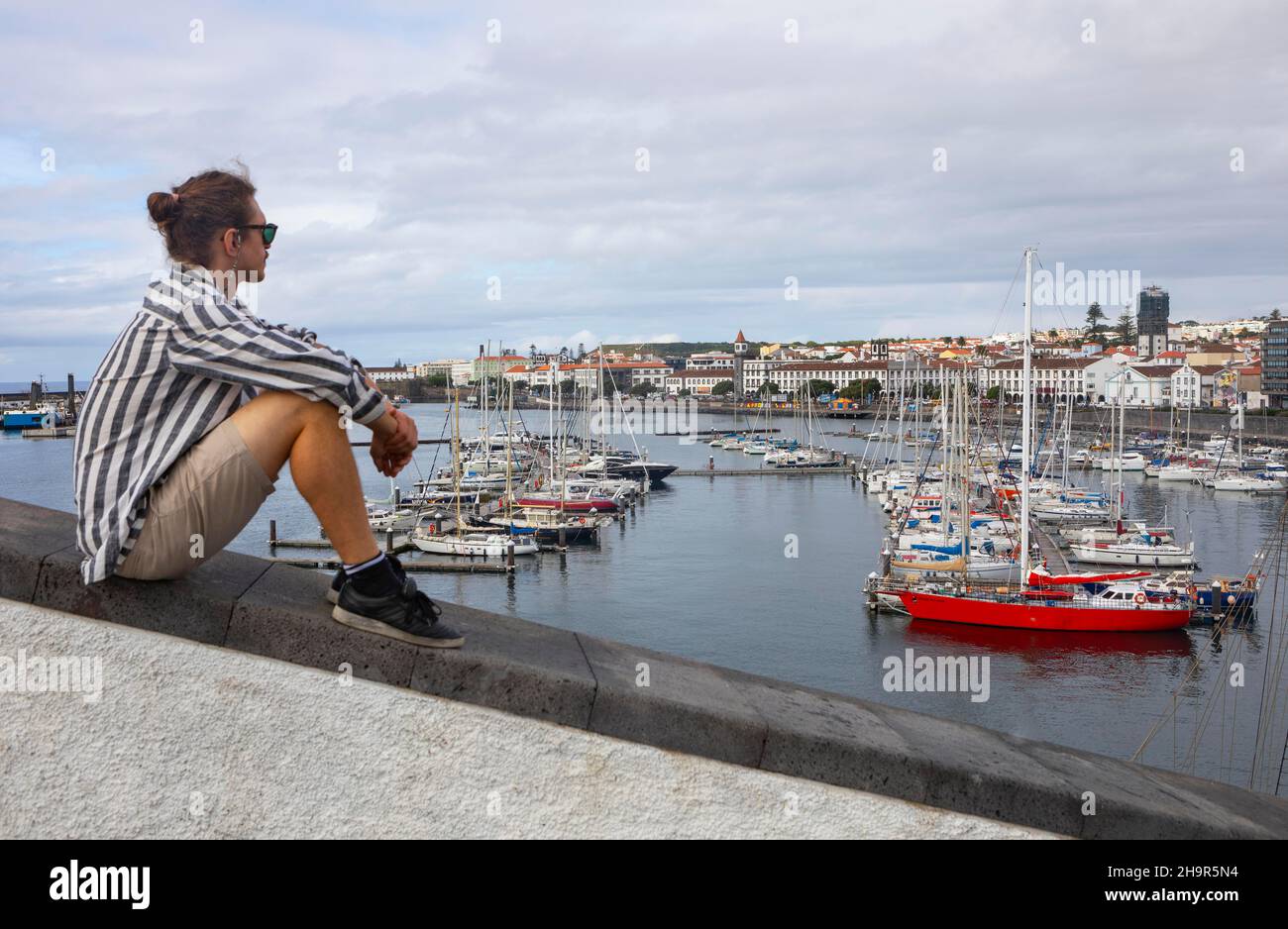 Junger Mann, der auf der Promenade in der Marina von Ponta Delgada, Sao Miguel Island, Azoren, Portugal, sitzt Stockfoto