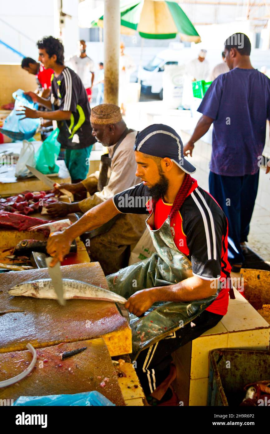 Männer entkalken die Fische gegen Bargeld und verarbeiten sie zu praktischen Einheiten mit großen Spaltmaschinen, Mutrah-Fischmarkt, Muscat, Oman Stockfoto