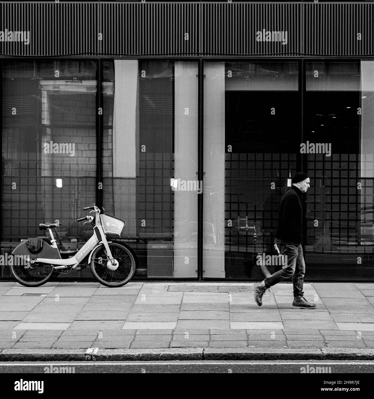 Central London Großbritannien November 21 2021, Mann, der alleine am Bürofenster vorbei mit dem geparkten Lime Pedal Hire Bike Victoria Steet London geht Stockfoto