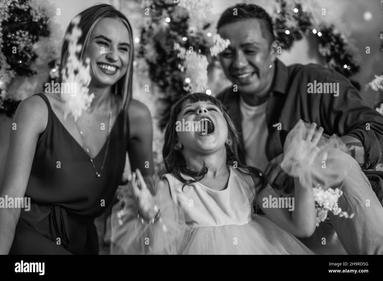 Weihnachts-Shooting. Neujahrsfoto der glücklichen Familie mit schöner Tochter. Mann, Frau und nettes Mädchen spielen mit künstlichem Schnee. Schwarz-Weiß-Bild Stockfoto