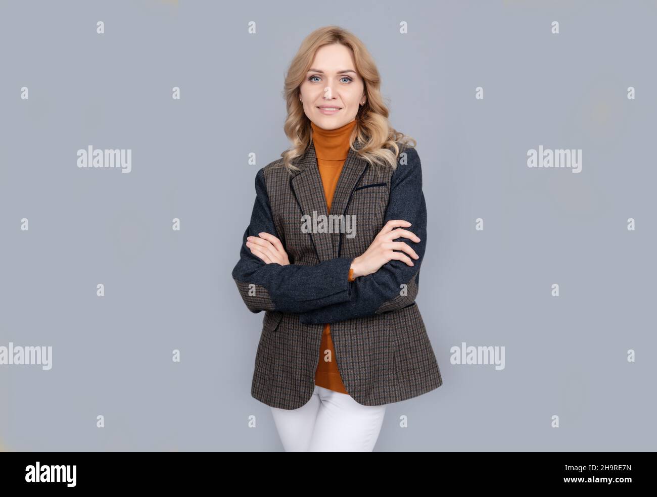 Lächelnde Geschäftsfrau in englischer Kleidung auf grauem Hintergrund. Fröhliche blonde Frau in Jacke Stockfoto