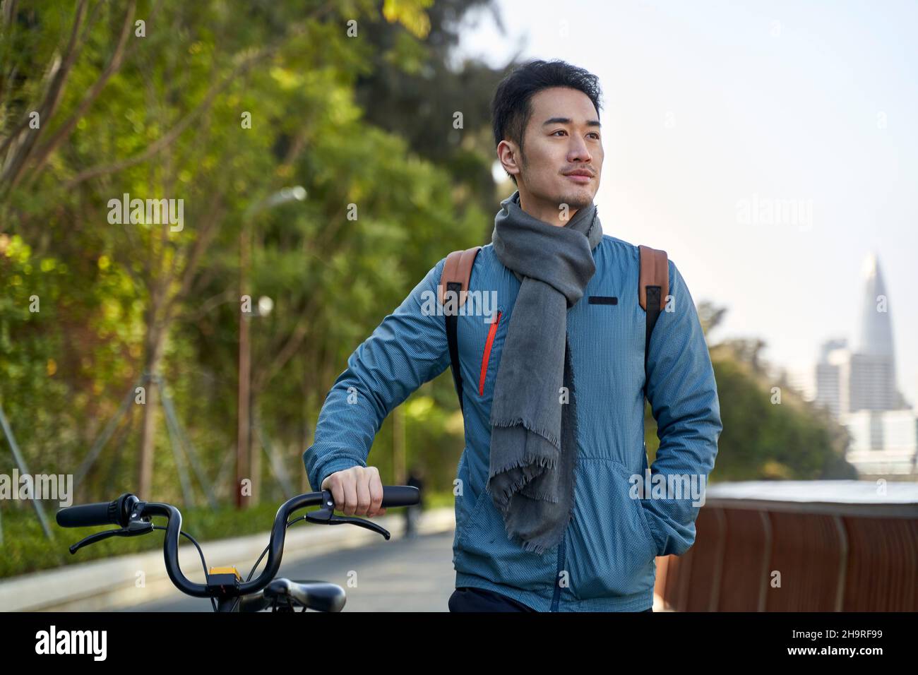 Junger asiatischer Mann, der in der modernen Stadt mit dem Fahrrad im öffentlichen Park spazieren geht Stockfoto