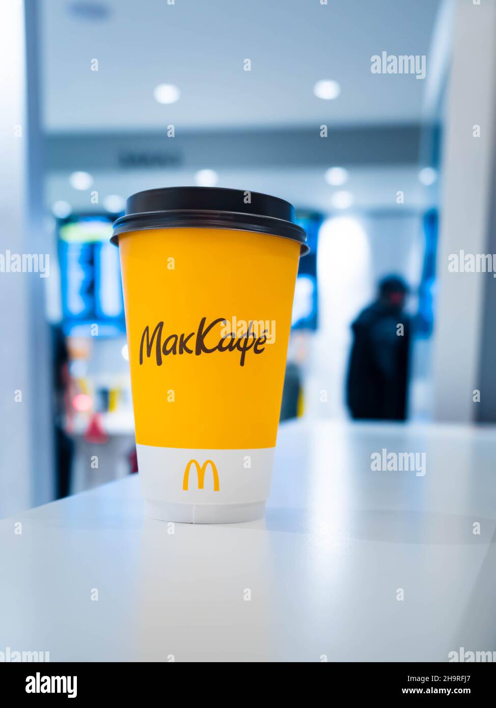 Moskau, Russland - 3. April 2021: Eine gelbe Tasse Kaffee auf dem Tisch bei McDonalds stehen die Leute vor dem Hintergrund am Kundenserviceschalter. Der Stockfoto