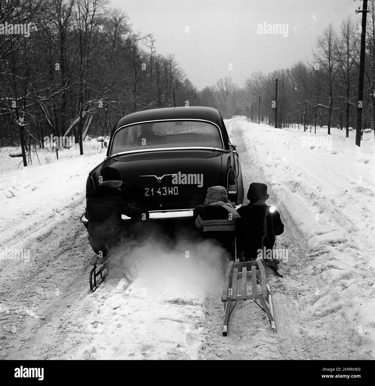 Polska, 1970. Dzieci na sankach przyczepionych do samochodu Wo³ga GAZ-21 na zaœnie¿onej drodze. ³p PAP/Edmund Uchymiak Dok³adny miesi¹c i dzieñ wydarzenia nieustalone. Polen, 1970. Kinder auf einem Schlitten, der am Wolga GAZ-21 Auto auf einer schneebedeckten Straße befestigt ist. lp PAP/Edmund Uchymiak Stockfoto