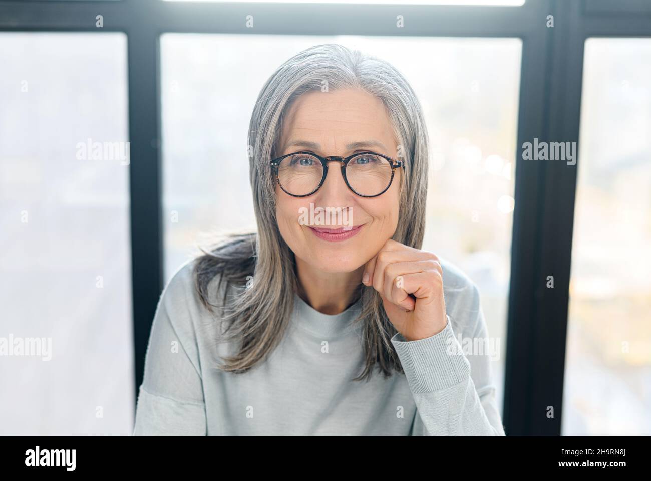 Eine positive Geschäftsfrau, die eine elegante Brille trägt, blickt auf die Kamera und lächelt. Nahaufnahme des Porträts einer selbstbewussten grauhaarigen Frau, einer reifen Lehrerin, einer geschäftsführerin, einer erfahrenen Managerin Stockfoto