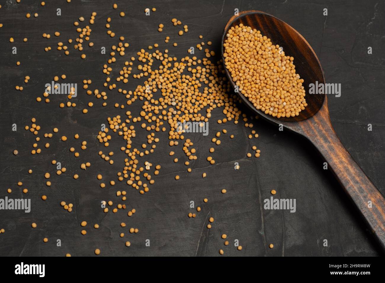 Yellow Raw Organic Senf Seeds auf Holzlöffel auf dunklem Beton Hintergrund Stockfoto