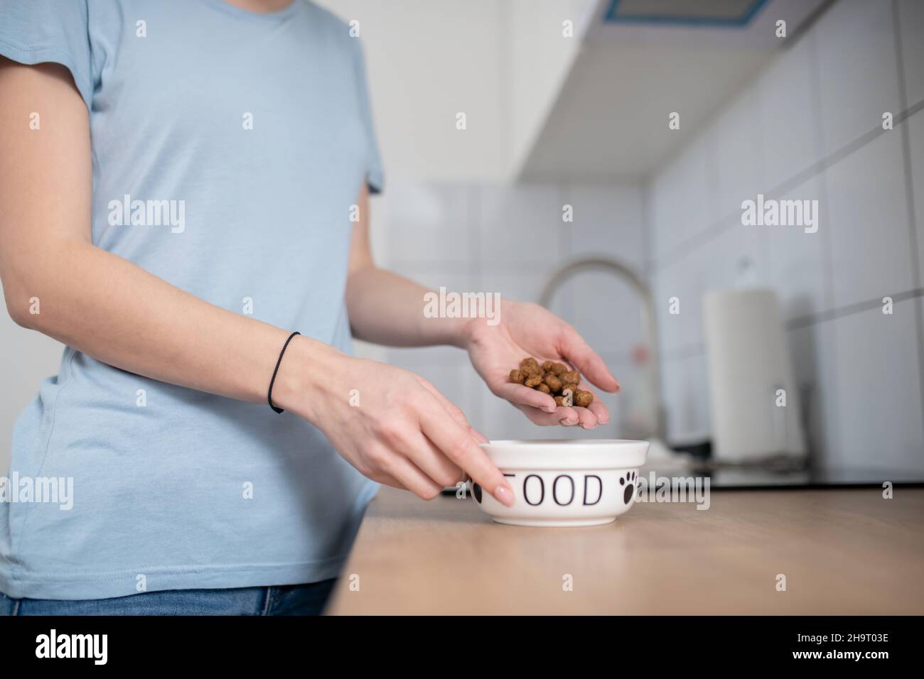Eine Frau hält eine Handvoll Pellets über eine Keramikschale Stockfoto
