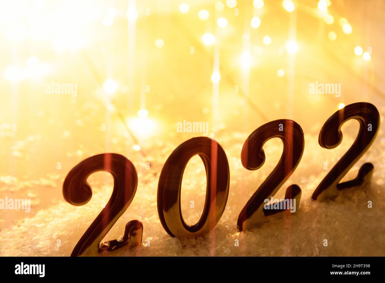 Goldzahlen 2022 auf gelbem Hintergrund mit anamorphem Filter und leuchtender Girlande. Neujahr im Hintergrund mit 2022 Jahren Stockfoto