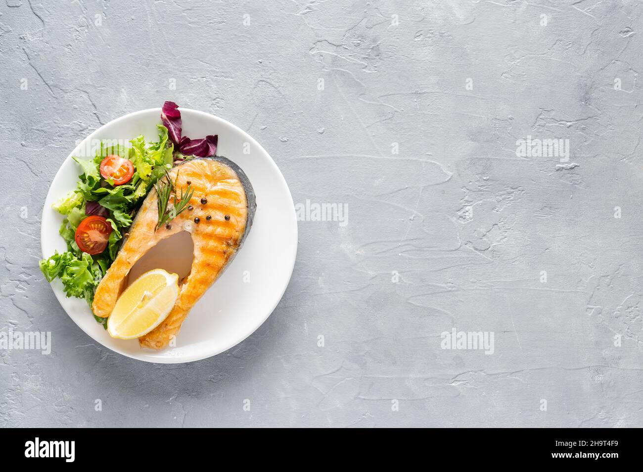 Gegrilltes Lachsfischsteak mit Salat und Tomaten auf einer weißen Keramikplatte Stockfoto