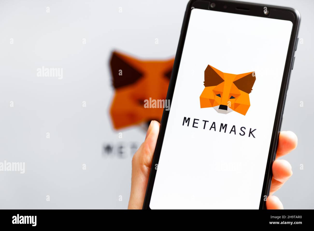 Ukraine, Odessa - Oktober, 9 2021: Hand hält Handy mit MetaMask App läuft auf dem Smartphone-Bildschirm mit MetaMask Logo im Hintergrund. MetaMask ist eine Software-Krypto-Geldbörse Stockfoto