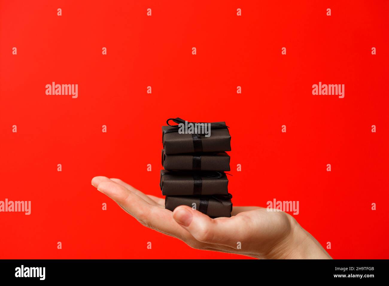 Weibliche Hand hält kleine schwarze Geschenk-Boxen mit schwarzen Bändern auf hellem sattem rotem Hintergrund Stockfoto