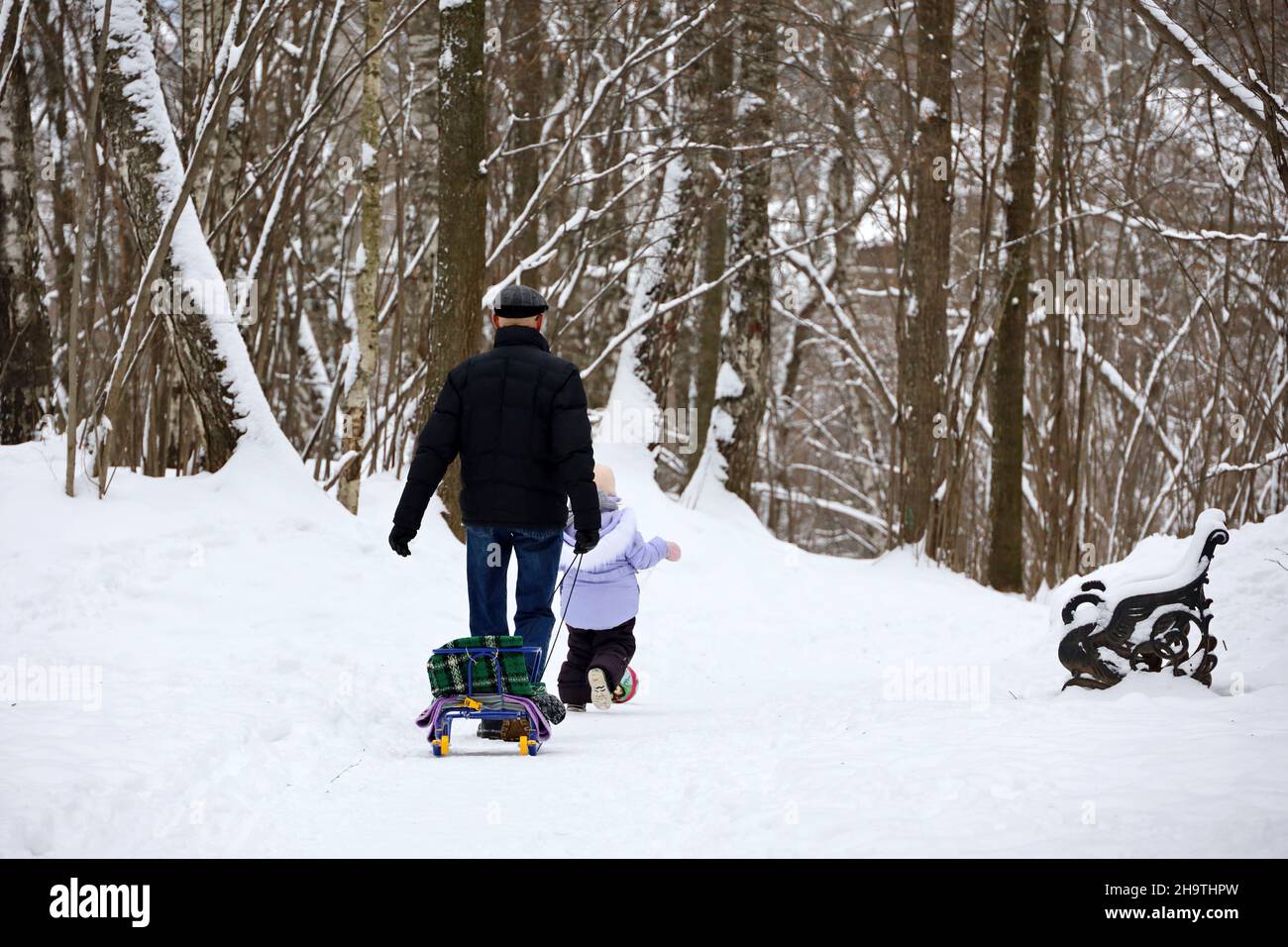 Familienfreizeit im Winterpark, Mann mit Schlitten, der mit einem Kind durch den Schnee läuft. Vater mit Kind, Natur nach Schneefall Stockfoto