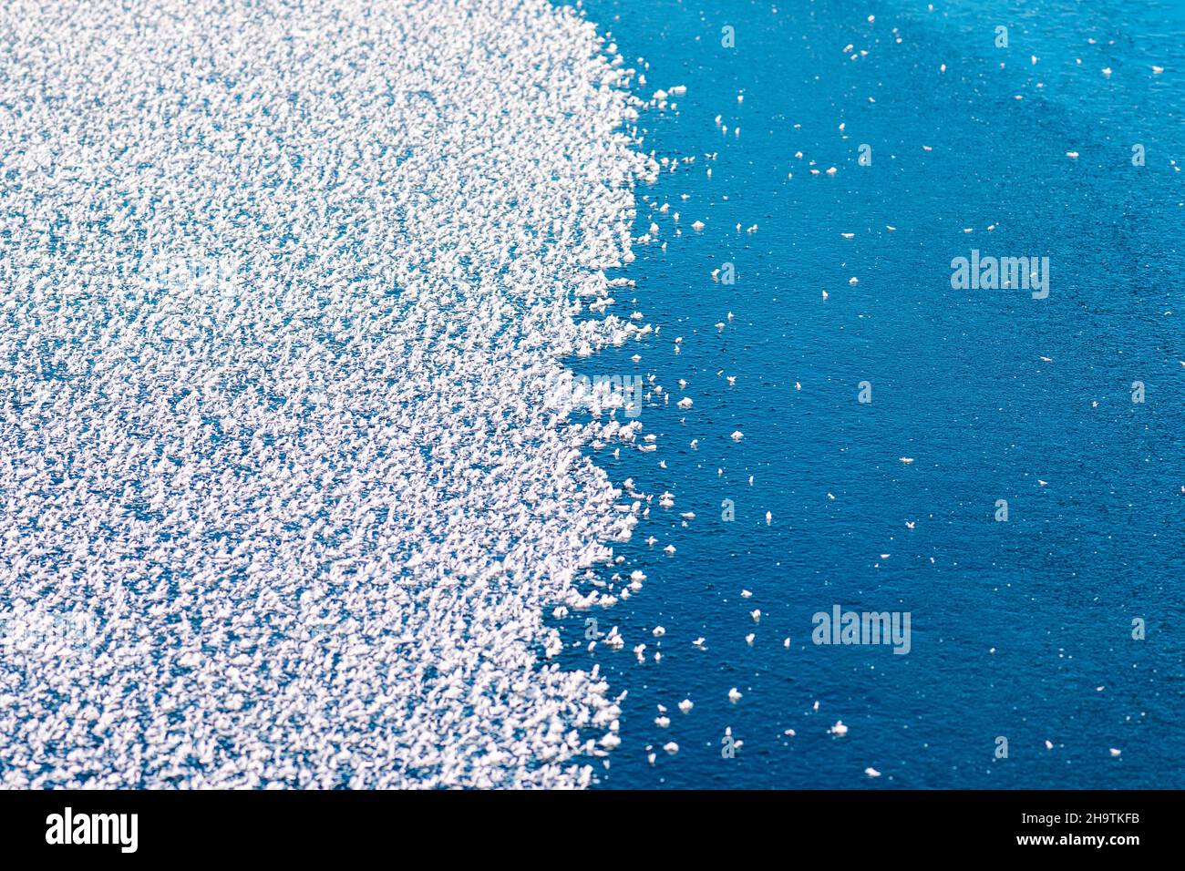 Oberfläche eines gefrorenen Sees, halb mit Schneeflocken bedeckt, halb blau Stockfoto