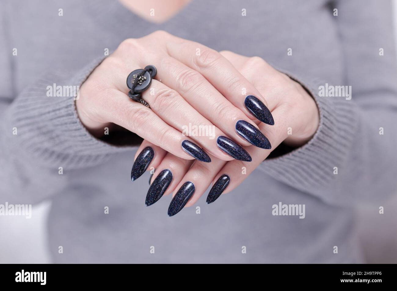 Weibliche Hand mit langen Nägeln und dunkelblauer schwarzer Maniküre hält  eine Flasche Nagellack Stockfotografie - Alamy