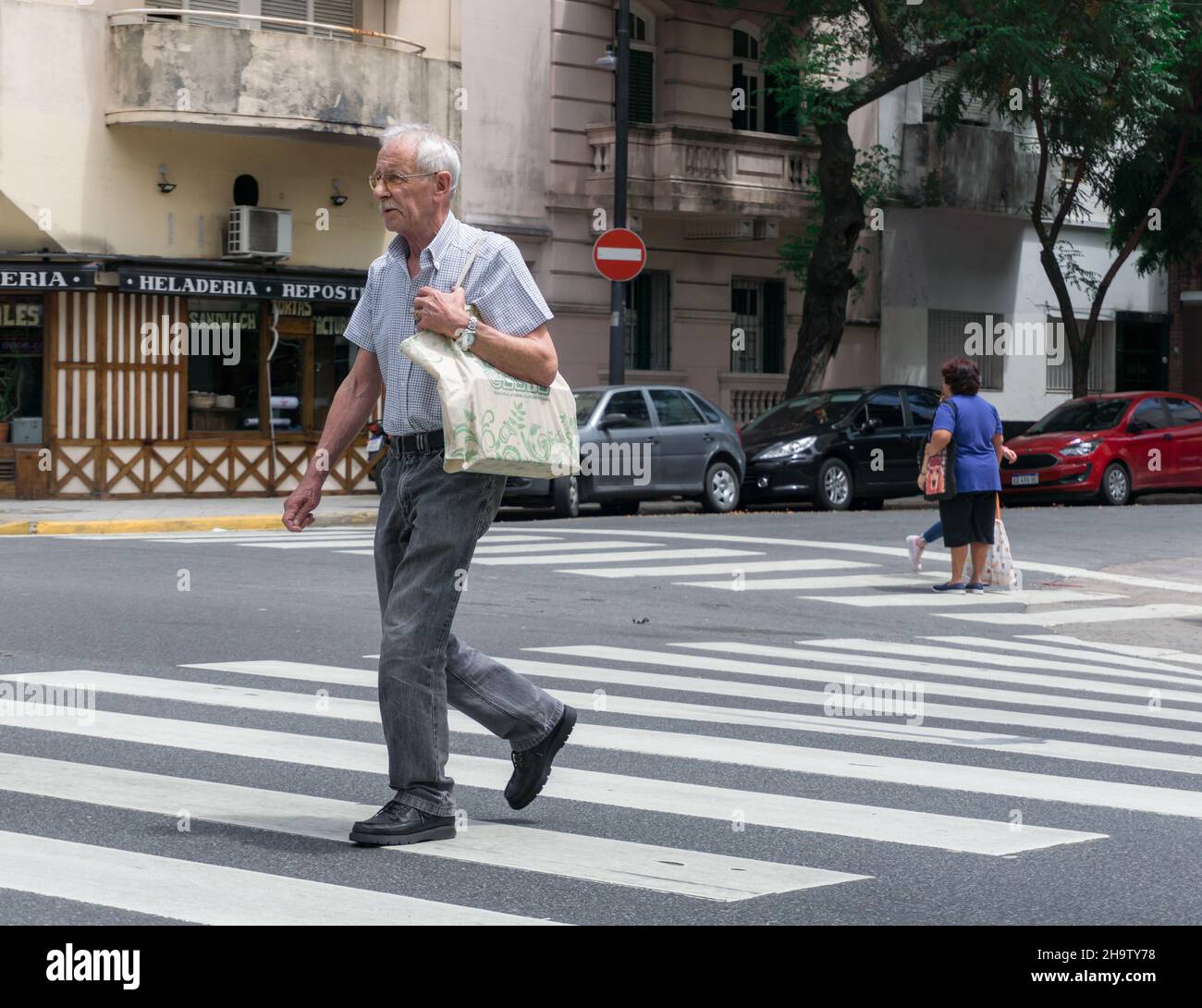Buenos Aires, Argentinien. 22. November 2019: Ein alter Mann geht mit einer Einkaufstasche in Buenos Aires über die Zebrakreuzung Stockfoto