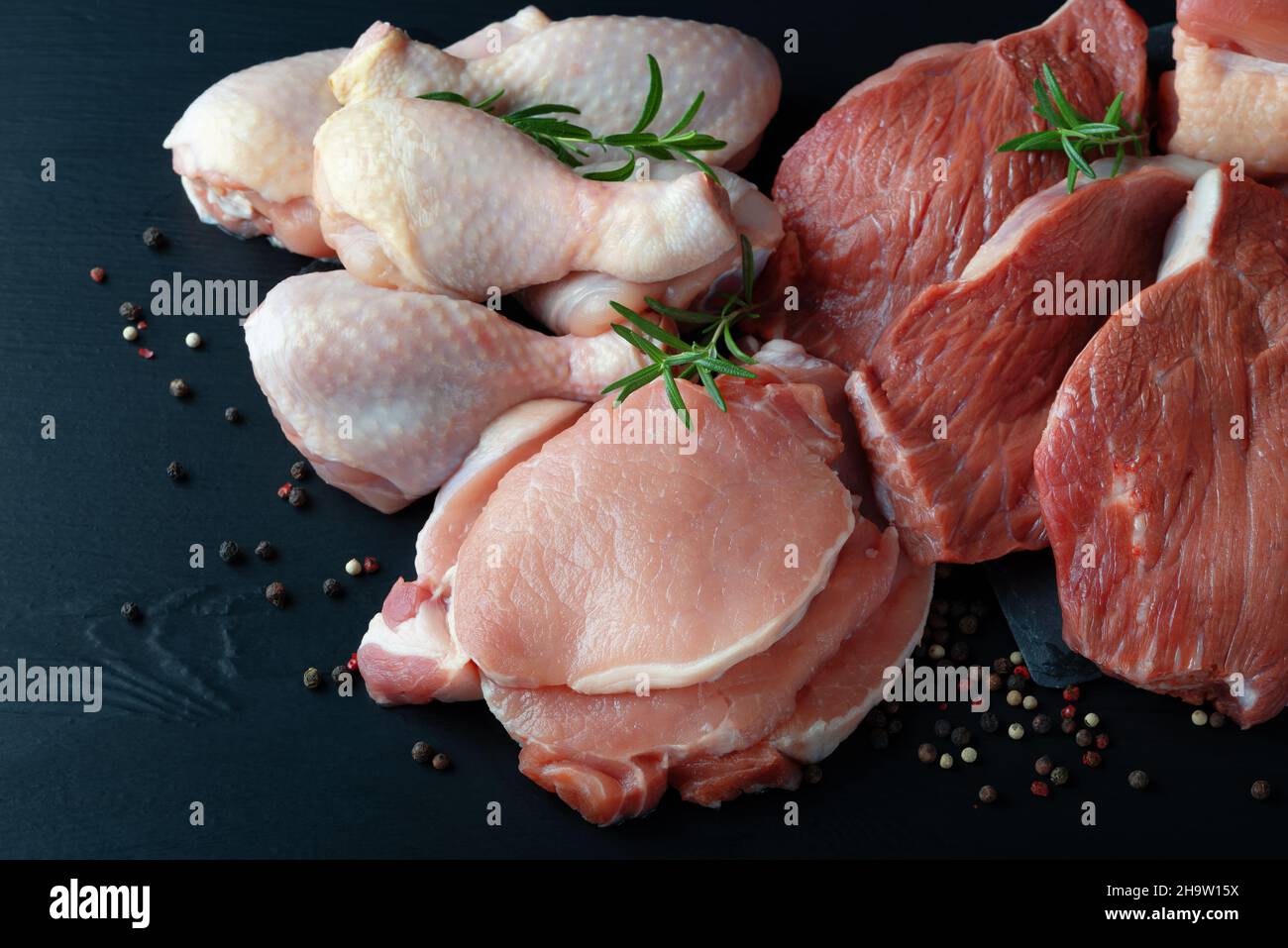 Verschiedene Arten von frischem Fleisch: Schweinefleisch, Rindfleisch und Huhn auf einem schwarzen Tisch Stockfoto