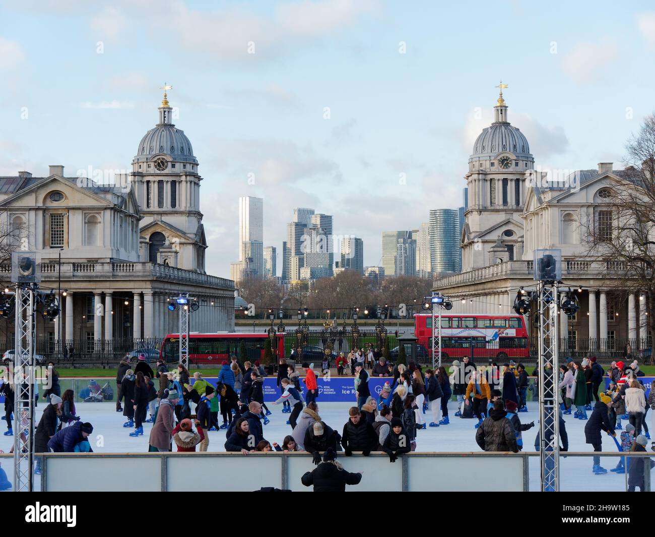 Eislaufen in Greenwich mit den Universitätsgebäuden dahinter und den Wolkenkratzern von Canary Wharf in der Ferne. Stockfoto