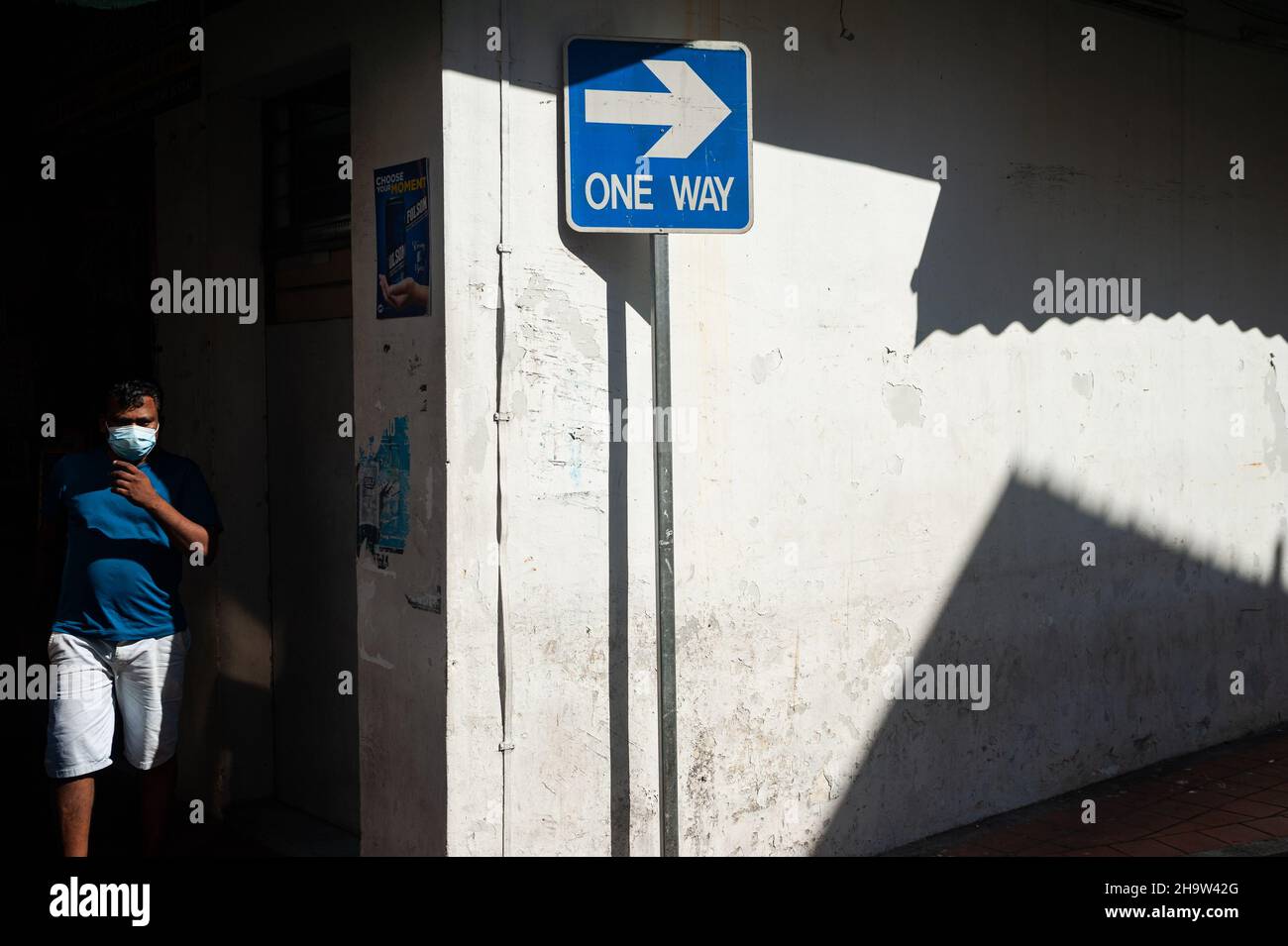 '27.10.2021, Singapore, , Singapur - die alltägliche Szene zeigt einen Mann mit einem Mundschutz, der neben einem Einbahnstraßenschild in der Little India neig steht Stockfoto