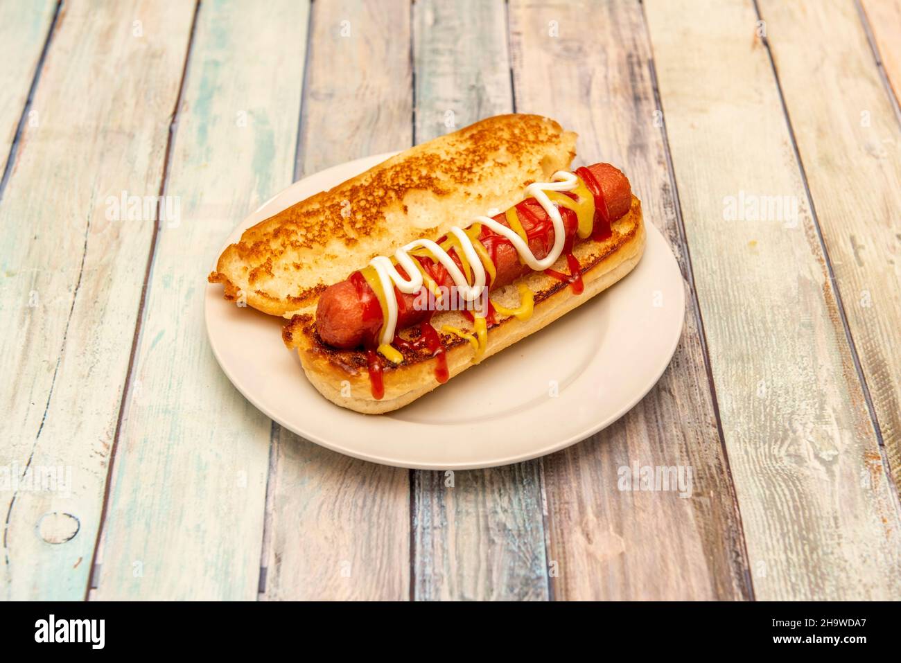 Klassischer Hot Dog mit Senf, Ketchup und Mayonnaise auf geröstetem Brioche-Brot Stockfoto