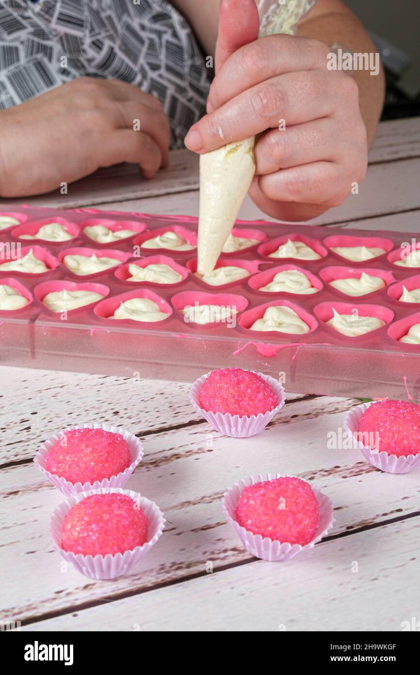 Bicho de pe, brasilianische Süßigkeiten. Im Hintergrund ein Bäcker, der Bonbons mit Ganache füllt (vertikales Foto). Stockfoto